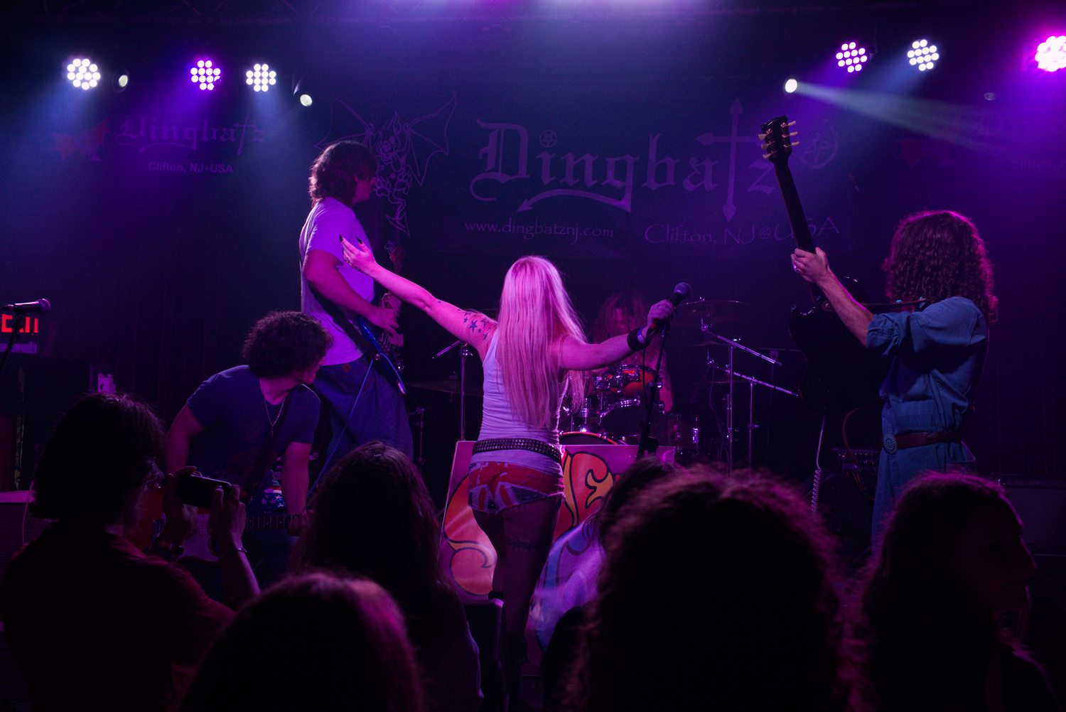 Dingbatz mid-set, the singer turned upstage towards her band with her arm flung out, the guitarists either side of her and the crowd silhouetted across the foreground